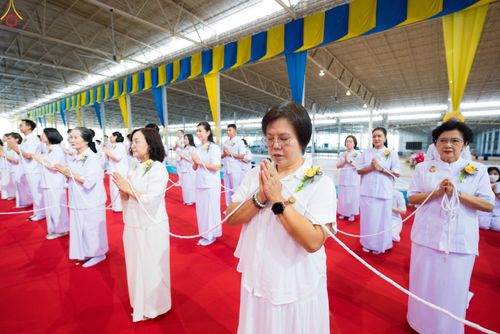 กลุ่มคนสวมชุดขาวกำลังพนมมือถือสายสิญจน์ในพิธีทางศาสนา