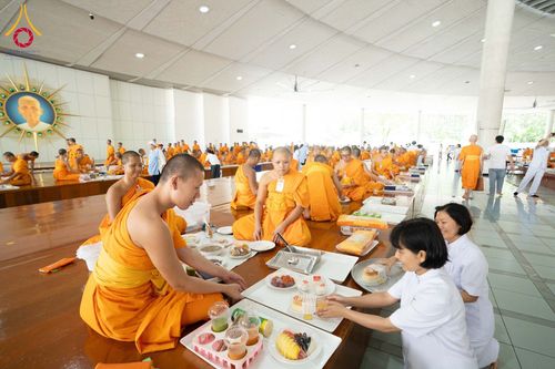 พระภิกษุสงฆ์และอุบาสิกาในชุดขาวกำลังจัดเตรียมภัตตาหารบนโต๊ะภายในหอฉันขนาดใหญ่
