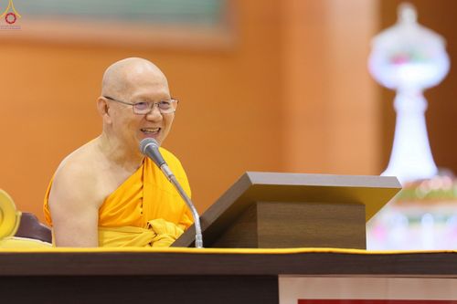 พระภิกษุสงฆ์สวมแว่นตากำลังพูดผ่านไมโครโฟนด้วยรอยยิ้มในระหว่างการแสดงธรรม
