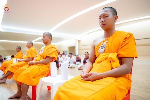 พระภิกษุสงฆ์หลายรูปนั่งสมาธิเรียงแถวกันภายในห้องโถงปฏิบัติธรรม