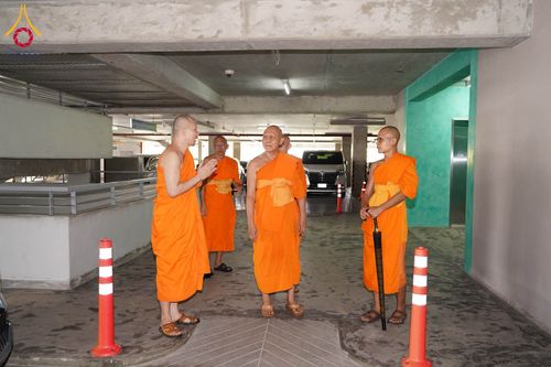 พระภิกษุสงฆ์หลายรูปกำลังเดินสำรวจและสนทนากันภายในอาคารจอดรถ