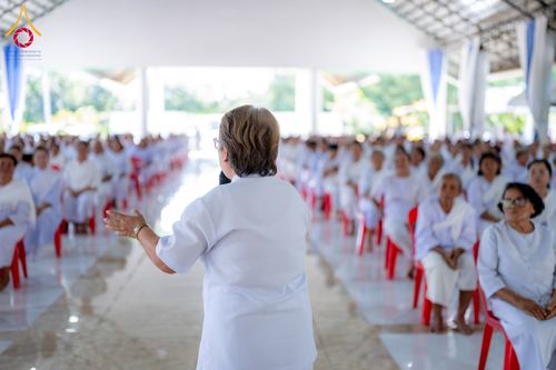 วิทยากรยืนบรรยายธรรมให้ผู้เข้าร่วมโครงการในชุดสีขาวนั่งฟังอย่างตั้งใจภายในอาคาร