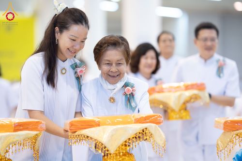 กลุ่มคนในชุดสีขาวกำลังถือพานพุ่มผ้าไตรในพิธีทางศาสนา
