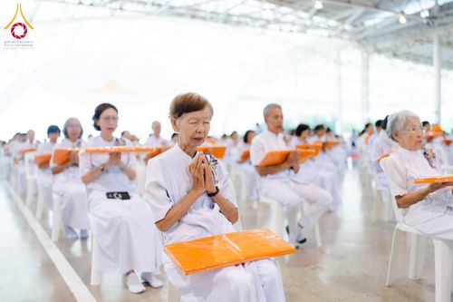 กลุ่มคนสวมชุดขาวนั่งพนมมือประกอบพิธีทางศาสนาภายในอาคาร