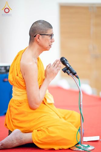 พระภิกษุสงฆ์นั่งพนมมือและพูดผ่านไมโครโฟนบนเวที