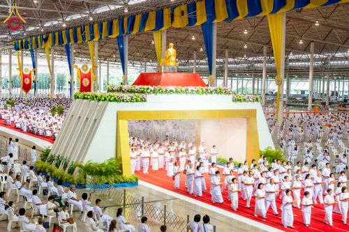 พุทธศาสนิกชนสวมชุดขาวเดินแถวในพิธีทอดผ้าป่าภายในอาคารขนาดใหญ่ที่มีการตกแต่งด้วยผ้าสีเหลืองและน้ำเงิน