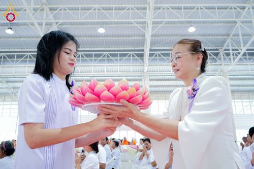หญิงสองคนสวมชุดสีขาวกำลังถือพานดอกบัวสีชมพูร่วมกันในพิธีทางศาสนา