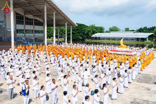 กลุ่มพุทธศาสนิกชนและพระสงฆ์จำนวนมากยืนร่วมพิธีอัญเชิญพระพุทธรูปประธานบนแท่นกลางลานกว้างหน้าอาคาร