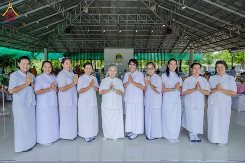 กลุ่มอุบาสิกาหญิงสวมชุดขาวพนมมือยืนเรียงแถวหน้ากระดานภายในอาคาร