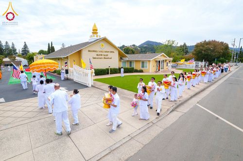 ขบวนพุทธศาสนิกชนชุดขาวเดินถือพานพุ่มและดอกไม้หน้าวัดพระธรรมกายซิลิคอนวัลเลย์
