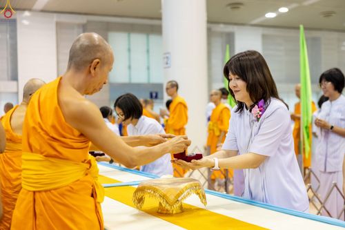 พระภิกษุกำลังมอบพระของขวัญให้แก่สุภาพสตรีชุดขาวในพิธี