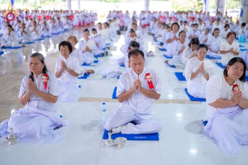 กลุ่มคนสวมชุดขาวนั่งพนมมือปฏิบัติธรรมในอาคาร