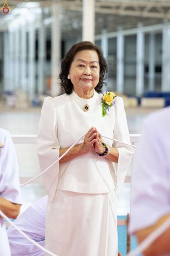 สุภาพสตรีสวมชุดสีขาวประนมมือไหว้ด้วยใบหน้ายิ้มแย้ม