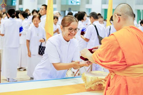 หญิงสวมชุดขาวกำลังรับมอบพระของขวัญจากพระภิกษุสงฆ์ในพิธีการ