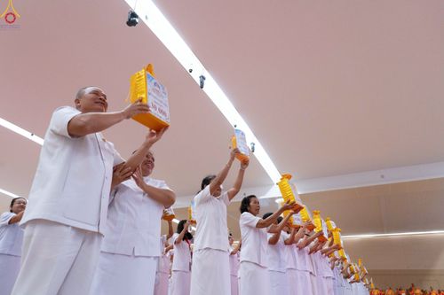 กลุ่มคนในชุดขาวกำลังยืนชูถุงสังฆทานสีเหลืองทองขึ้นเหนือศีรษะภายในอาคาร