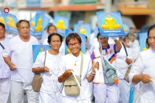 กลุ่มคนสวมชุดขาวถือป้ายรูปพระพุทธรูปและเชือกสีขาวเดินในขบวนพิธีทางศาสนา