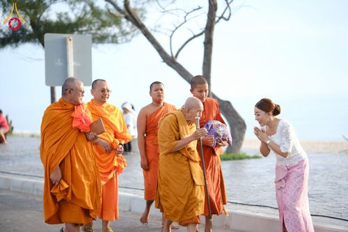 หญิงสาวสวมชุดไทยยกมือไหว้พระสงฆ์ขณะเดินบิณฑบาตริมชายหาด