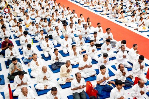 กลุ่มคนสวมชุดสีขาวนั่งพนมมือปฏิบัติธรรมบนเบาะรองนั่งในอาคาร
