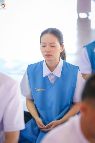 หญิงสาวสวมเสื้อกั๊กสีฟ้ากำลังนั่งหลับตาทำสมาธิ