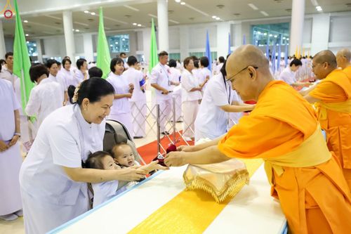 พระภิกษุสงฆ์มอบพระของขวัญให้เด็กเล็กโดยมีผู้ปกครองชุดขาวคอยดูแลในงานพิธี