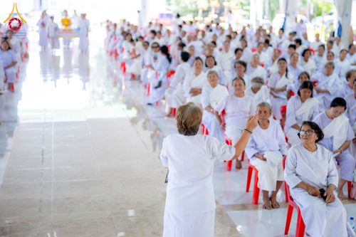 กลุ่มคนสวมชุดสีขาวนั่งฟังบรรยายในอาคารโดยมีวิทยากรยืนนำกิจกรรมอยู่ด้านหน้า