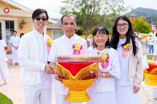 กลุ่มคนสวมชุดสีขาวถือพานพุ่มที่มีป้ายชื่อวัดพระธรรมกายซิลิคอนวัลเลย์ในงานพิธีทอดผ้าป่า