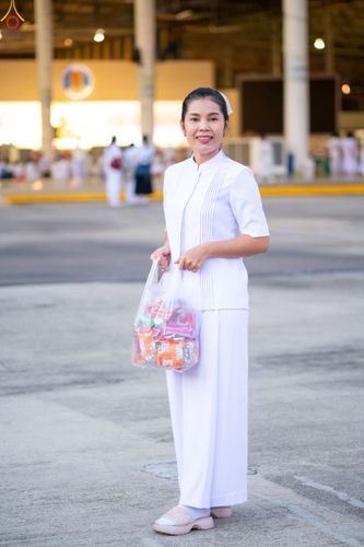 หญิงสาวสวมชุดสีขาวถือถุงอาหารแห้งยืนยิ้มให้กล้องในพื้นที่อาคารกว้างขวาง