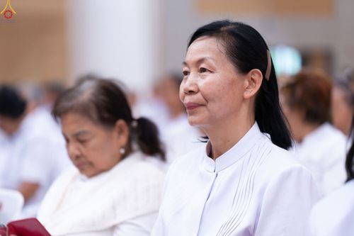 หญิงวัยกลางคนสวมชุดสีขาวนั่งฟังการบรรยายในห้องประชุม