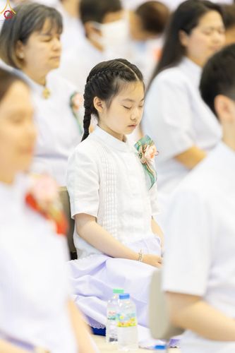 เด็กหญิงผมเปียสวมชุดสีขาวนั่งหลับตาทำสมาธิในพิธีทางศาสนา