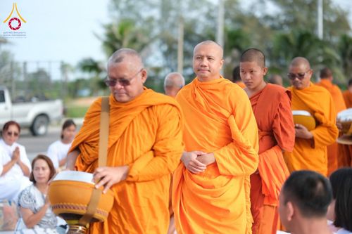 พระสงฆ์หลายรูปกำลังเดินรับบิณฑบาตโดยมีประชาชนนั่งรอใส่บาตรอยู่ด้านข้าง