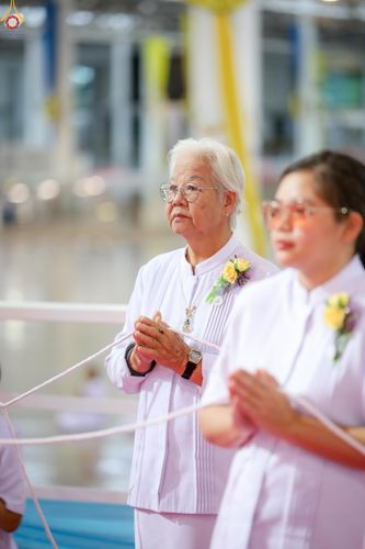หญิงสูงวัยสวมชุดขาวพนมมือถือสายสิญจน์ในพิธีทางศาสนา