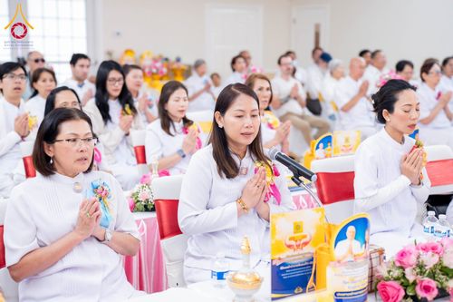 กลุ่มคนสวมชุดขาวนั่งพนมมือร่วมพิธีทางศาสนาภายในห้องโถง