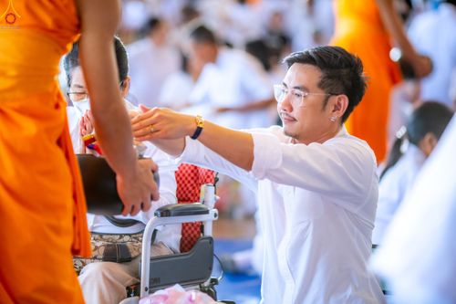 ชายหนุ่มสวมเสื้อสีขาวกำลังใส่บาตรพระภิกษุสงฆ์ในพิธีทำบุญ