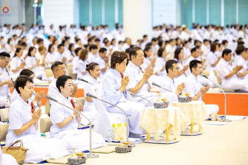 กลุ่มพุทธศาสนิกชนแต่งกายชุดสีขาวนั่งพนมมือร่วมพิธีทางศาสนาภายในอาคารขนาดใหญ่