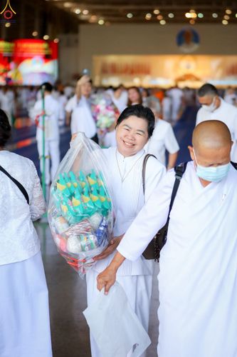 หญิงไทยสวมชุดขาวถือถุงใส่ของตักบาตรด้วยรอยยิ้มในพิธีทำบุญ