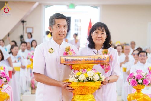 ชายและหญิงสวมชุดสีขาวถือพานพุ่มสีทองประดับดอกไม้ในพิธีทางศาสนา