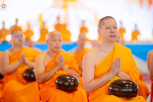 พระภิกษุสงฆ์หลายรูปนั่งพนมมือและมีบาตรวางอยู่ด้านหน้าในพิธีทางศาสนา