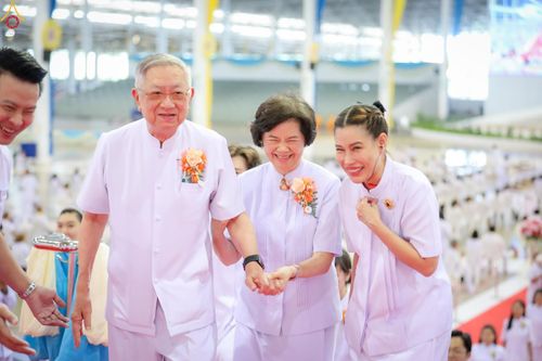 กลุ่มชายหญิงสวมชุดสีขาวกำลังเดินยิ้มแย้มแจ่มใสภายในงานพิธีที่มีผู้คนร่วมงานจำนวนมาก