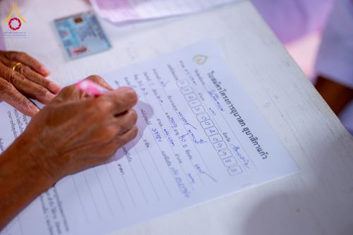 มือของผู้สมัครกำลังเขียนข้อมูลลงในใบสมัครโครงการอุบาสกแก้ว-อุบาสิกาแก้ว