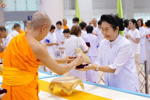 พระภิกษุสงฆ์มอบพระของขวัญให้แก่สุภาพสตรีในชุดสีขาวท่ามกลางพุทธศาสนิกชนภายในอาคาร