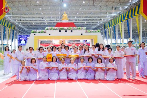 กลุ่มพุทธศาสนิกชนสวมชุดสีขาวถือพานผ้าป่าเรียงแถวถ่ายภาพร่วมกันภายในอาคารสภาธรรมกายสากล