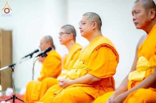 พระสงฆ์หลายรูปนั่งสมาธิเรียงแถวในพิธีทางศาสนาโดยมีไมโครโฟนตั้งอยู่ด้านหน้า