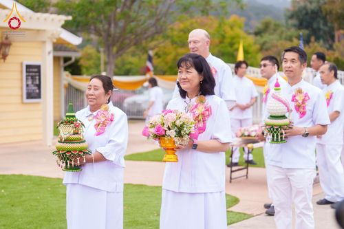 กลุ่มคนสวมชุดขาวถือพานพุ่มและพานดอกไม้เดินในขบวนพิธีทางศาสนา