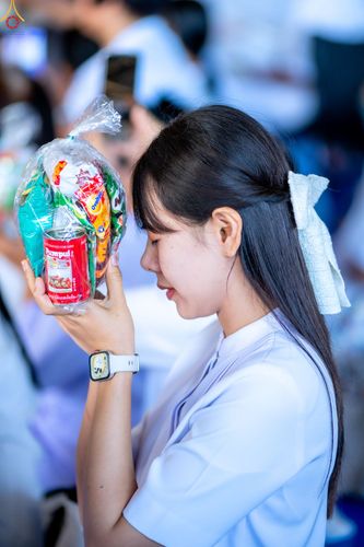 หญิงสาวผมยาวสวมชุดสีขาวถือถุงอาหารแห้งและกระป๋องอาหารเพื่อเตรียมตักบาตร