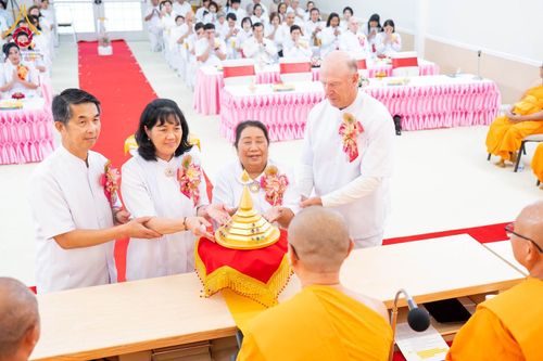 กลุ่มคนในชุดขาวกำลังประกอบพิธีอัญเชิญพระบรมสารีริกธาตุต่อหน้าพระภิกษุสงฆ์ในงานพิธีทางศาสนา