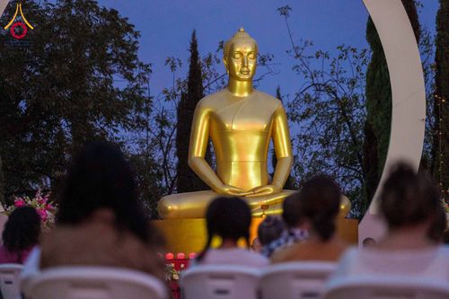 ผู้คนนั่งสมาธิเบื้องหน้าพระพุทธรูปสีทองขนาดใหญ่ในยามค่ำคืน