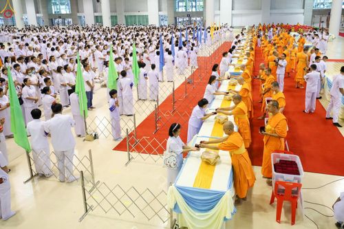 พระภิกษุสงฆ์กำลังมอบพระของขวัญให้แก่พุทธศาสนิกชนที่สวมชุดสีขาวภายในห้องโถงขนาดใหญ่