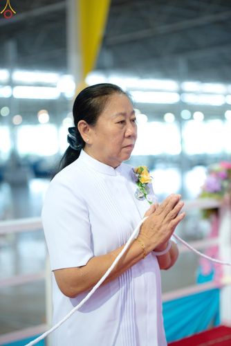 หญิงวัยกลางคนสวมชุดสีขาวพนมมือถือสายสิญจน์ด้วยท่าทางสำรวม
