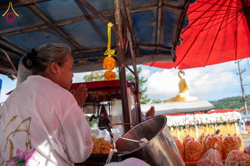 หญิงสูงวัยพนมมือไหว้พระพุทธรูปองค์สีทองในบรรยากาศงานพิธีกลางแจ้ง