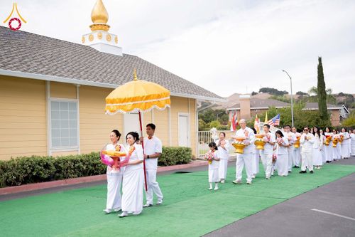 กลุ่มคนสวมชุดขาวเดินขบวนถือพานผ้าป่าและกางร่มสีเหลืองในพิธีกรรมทางศาสนา